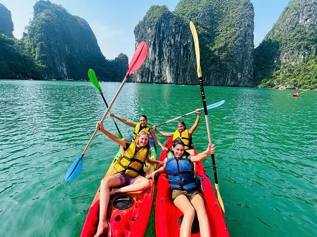 Four smiling women sitting in red and yellow kayaks raising their paddles
