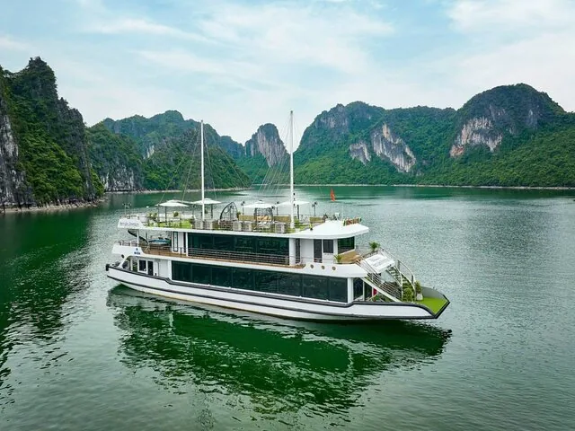 Multi-deck cruise boat anchored in a calm bay surrounded by limestone mountains