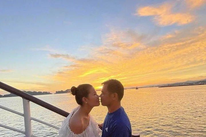 Couple about to kiss on a boat deck with a beautiful sunset background